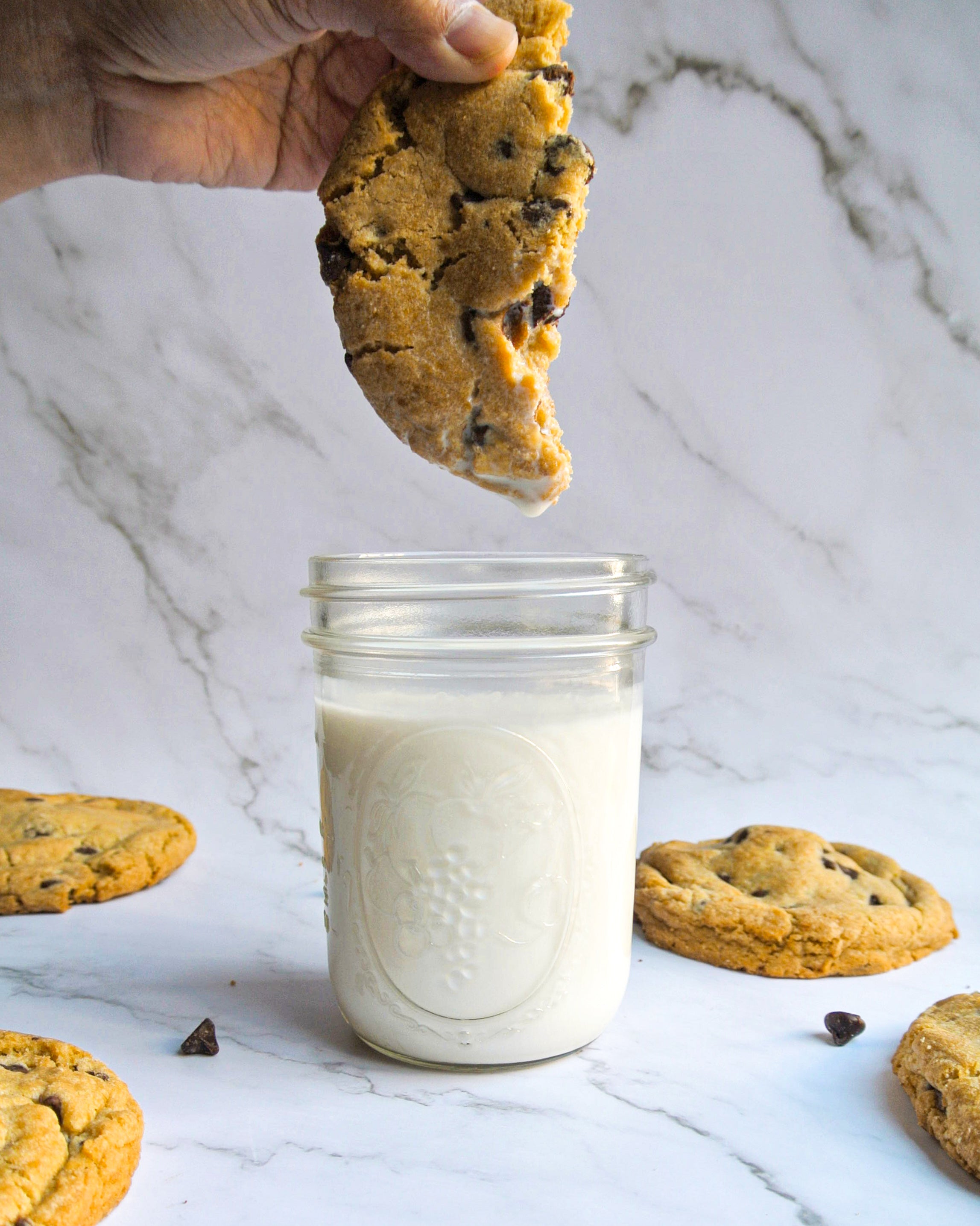 A warm chocolate chip cookie dripping after a dunk in a jar of cold milk